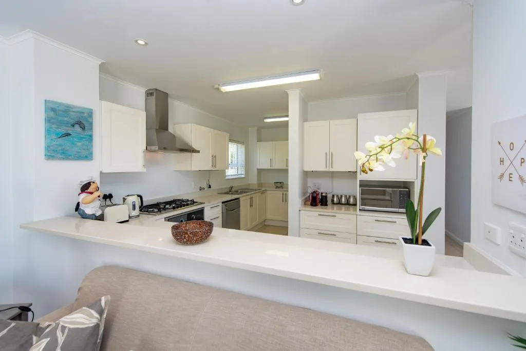 Modern open-plan kitchen with white cabinetry, stainless steel appliances, and white countertops