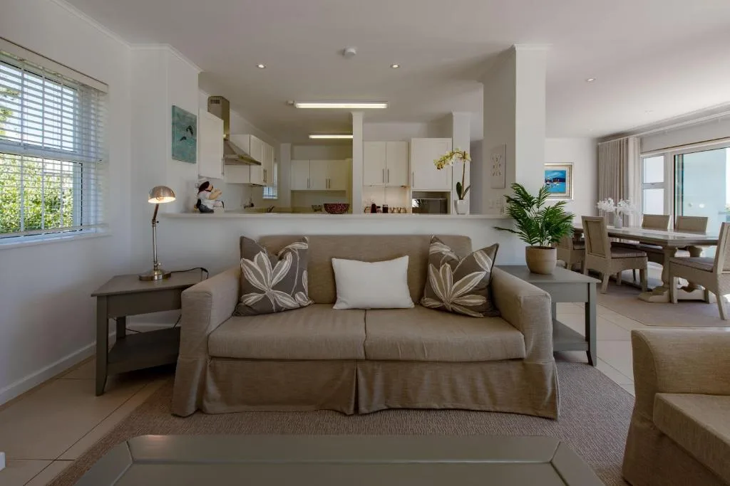 Bright lounge with beige sofa, decorative pillows, and open-plan kitchen beyond