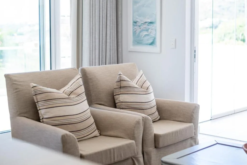 Bright lounge with beige armchairs, striped pillows, and ocean views