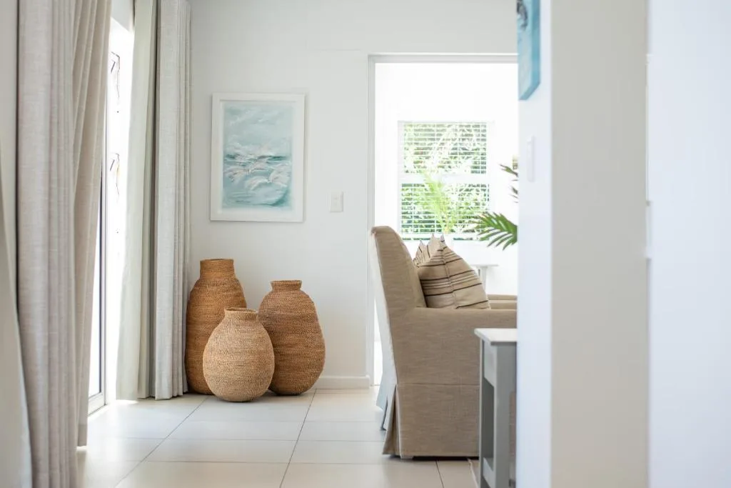 Bright lounge with cream armchair, woven baskets, and coastal artwork