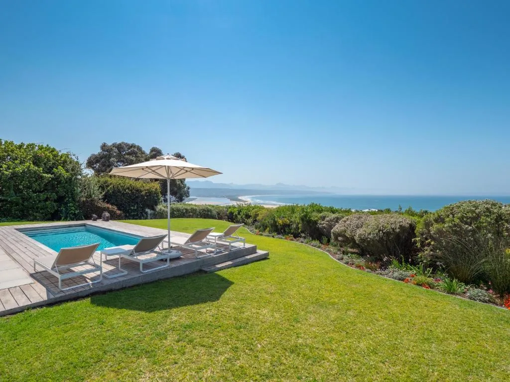 Swimming pool with loungers and ocean view beyond manicured garden