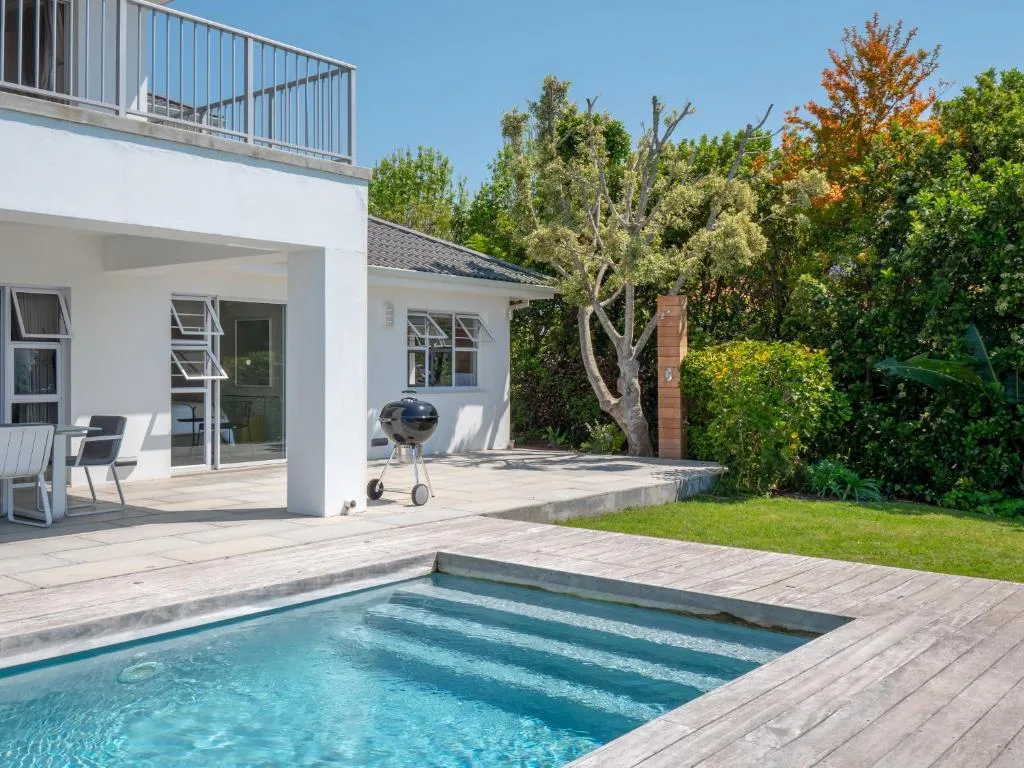 Swimming pool with wooden deck and modern white villa overlooking lush garden