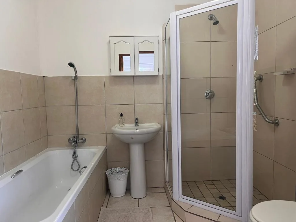 Compact bathroom with bathtub, pedestal sink, and walk-in shower enclosure