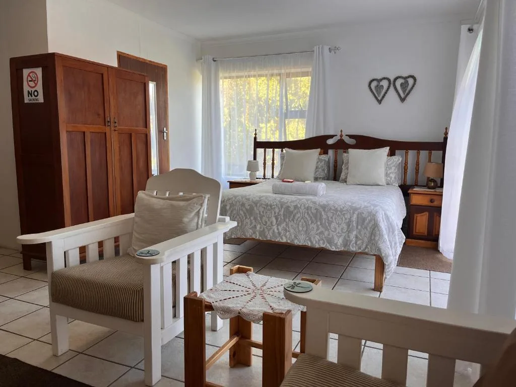 Bright bedroom with wooden bed, armchair, and garden views through windows