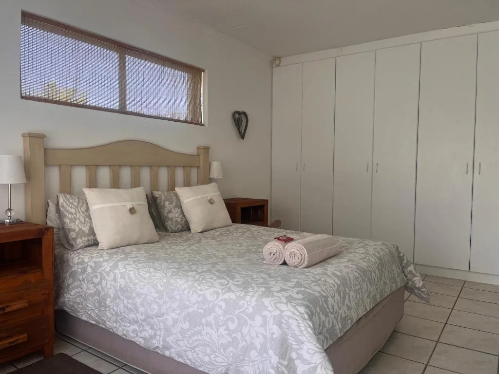 Bright bedroom with wooden bed frame, patterned bedding, and white built-in wardrobes