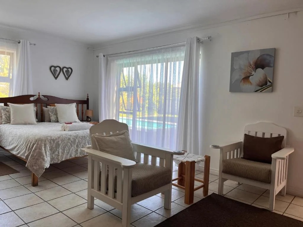 Bright bedroom with wooden bed, seating area, and garden views through glass doors
