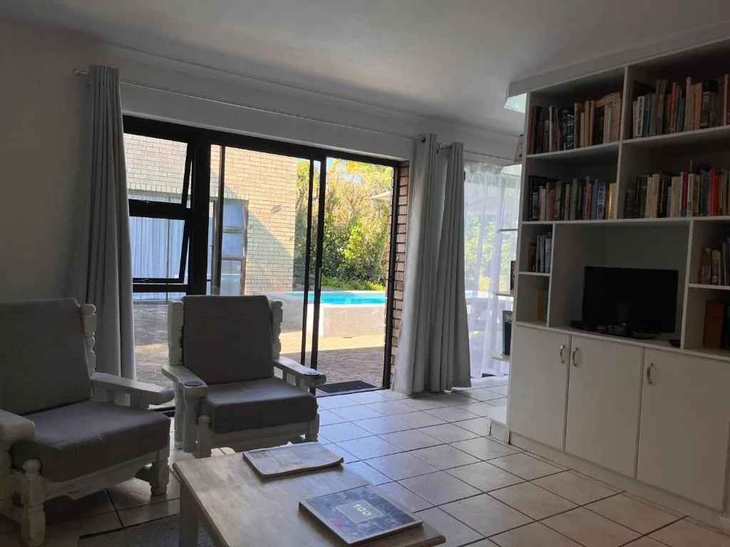 Bright living room with comfortable seating and built-in bookshelves overlooking pool