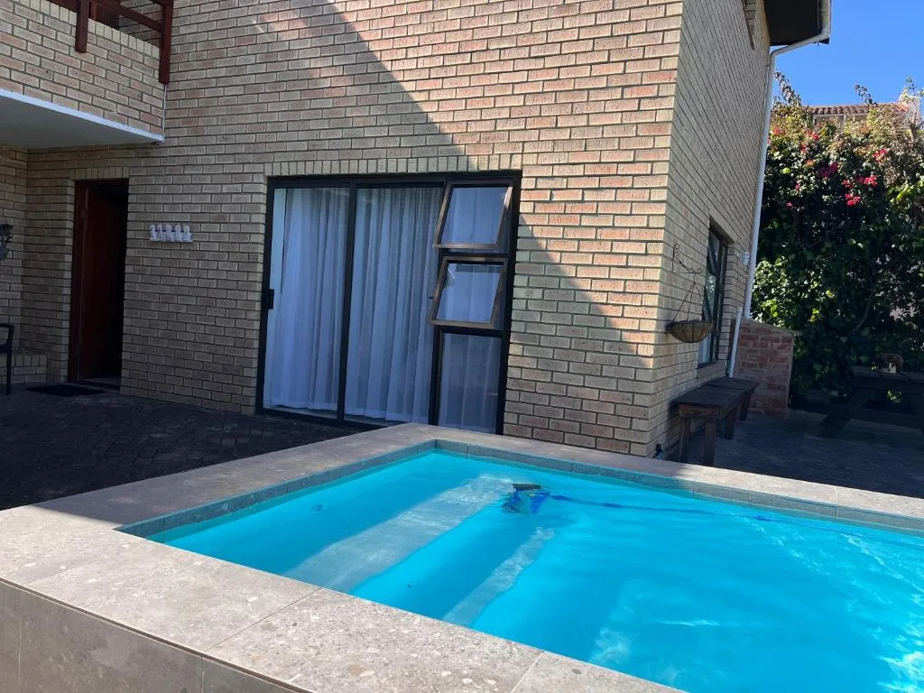 Bright blue swimming pool with brick house and garden backdrop