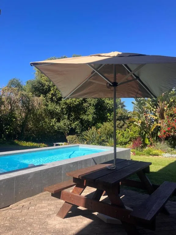 Swimming pool with large umbrella and wooden picnic table nearby