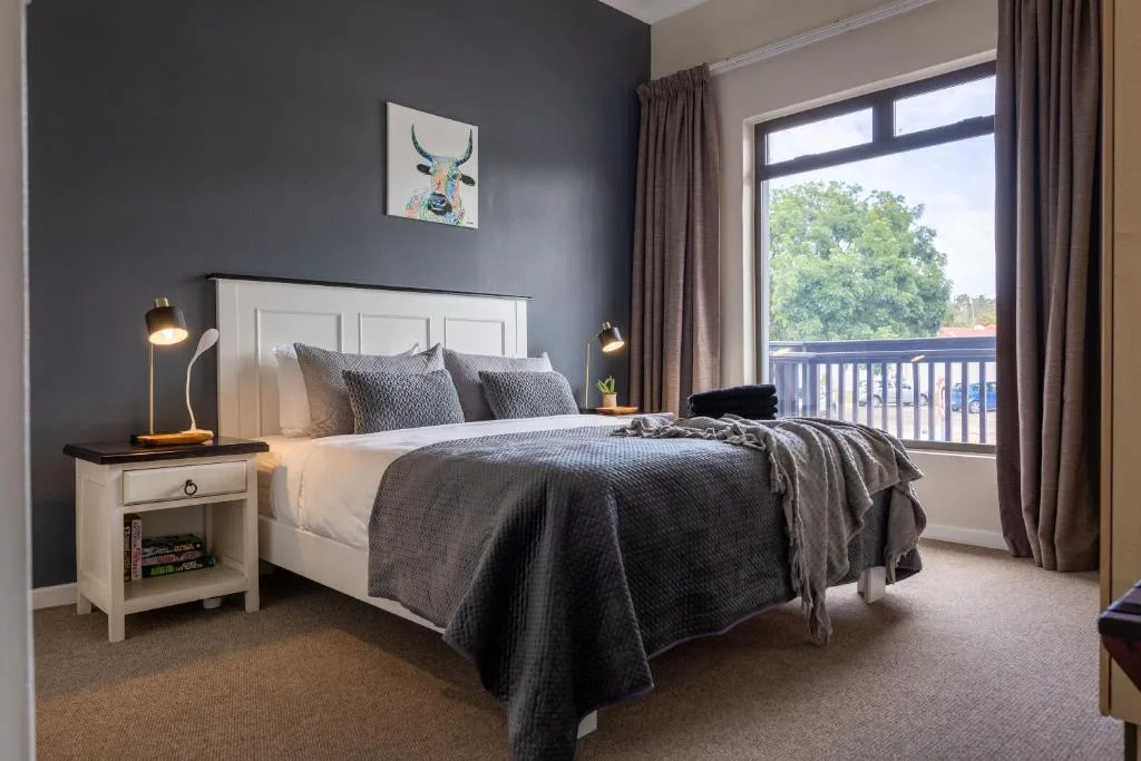 Modern bedroom with queen bed, dark accent wall, and balcony view of trees