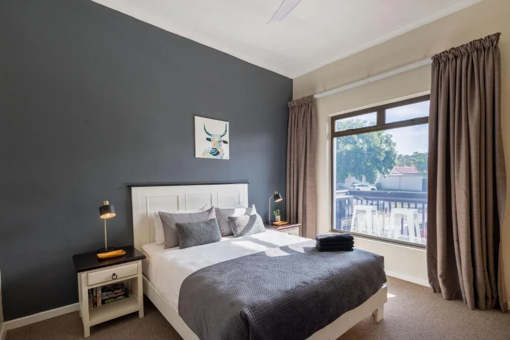 Modern bedroom with white headboard, dark accent wall, and large windows overlooking deck