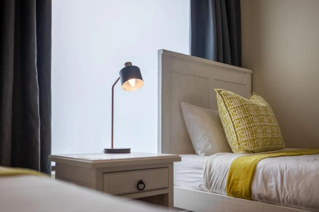Modern bedroom with bed, yellow pillows, and bedside lamp with window view