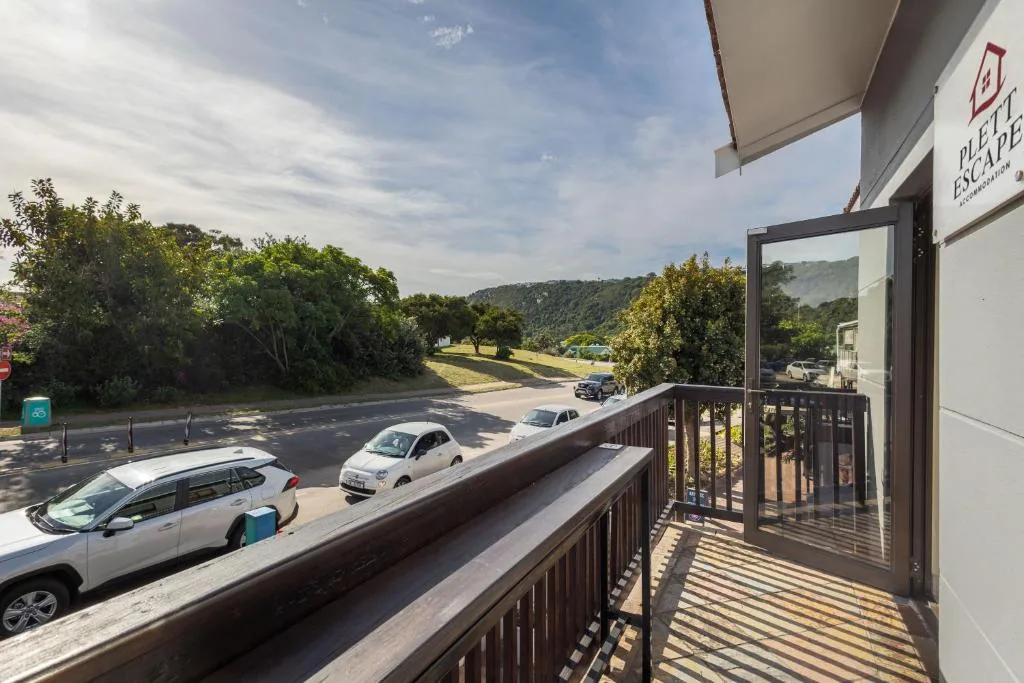 Wooden deck with glass railing overlooking parking area and green hills