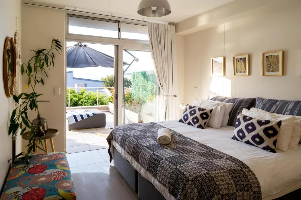 Bright bedroom with queen bed, patterned pillows, and deck access overlooking gardens