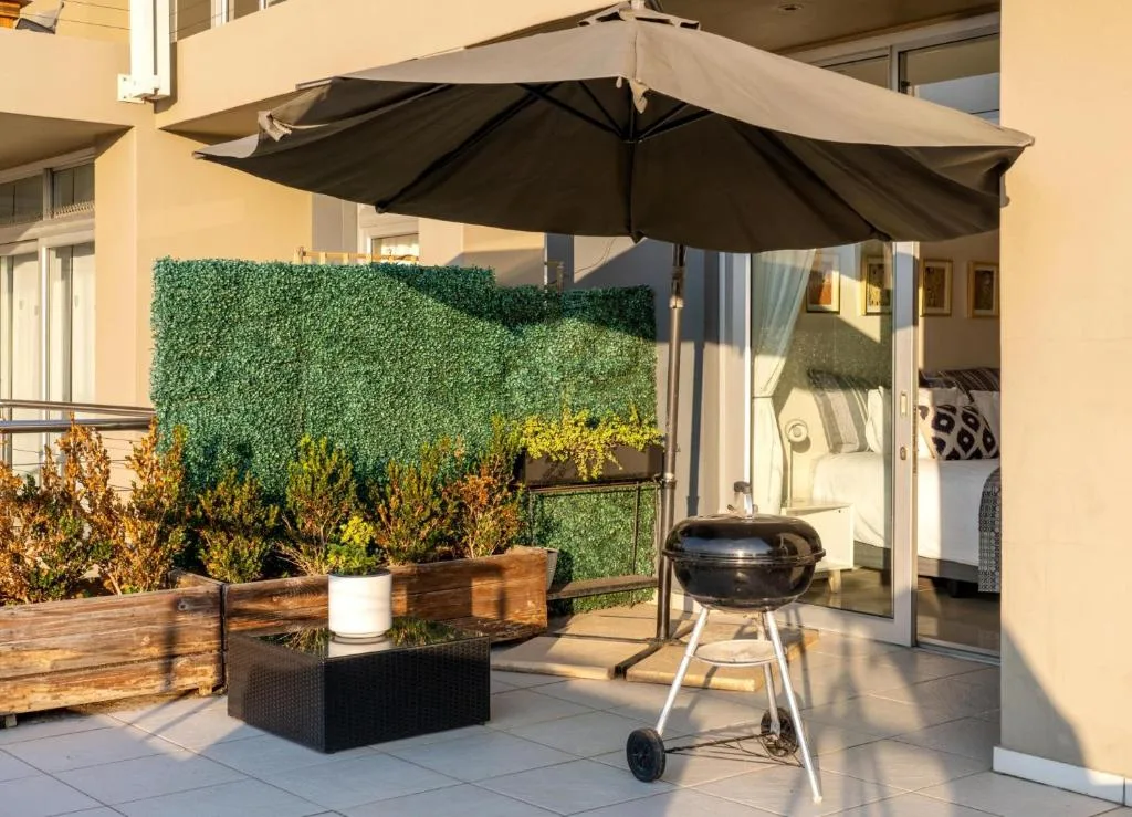 Sunny patio with black umbrella, braai grill, and potted plants