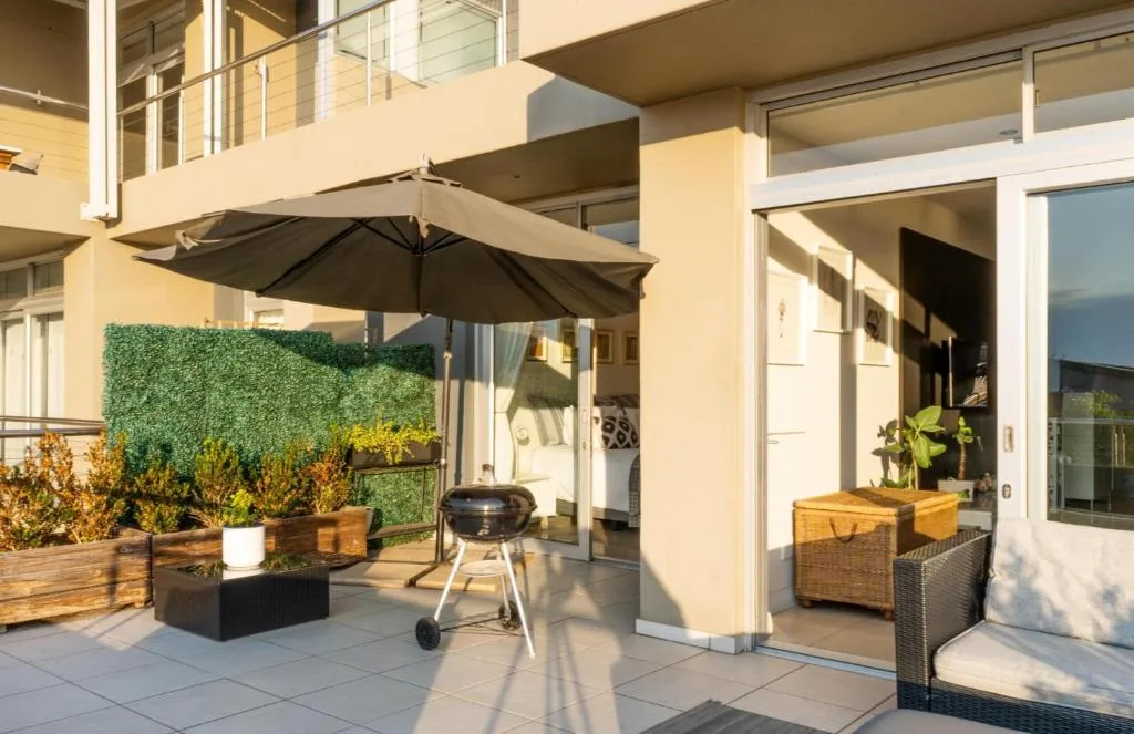Spacious patio with umbrella, braai grill, potted plants, and lounge seating