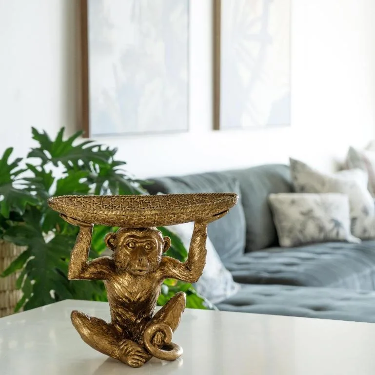 Gold monkey figurine holding tray on white surface, lounge visible behind
