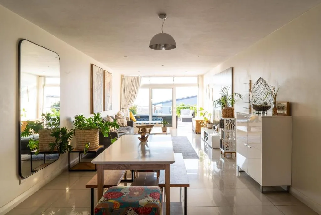 Bright open-plan lounge with dining table, plants, and sea views