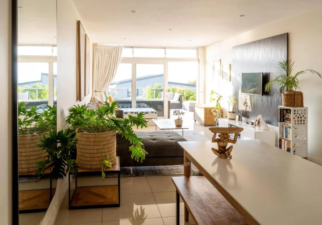 Bright open-plan lounge with sofa, potted plants, and ocean views through large windows