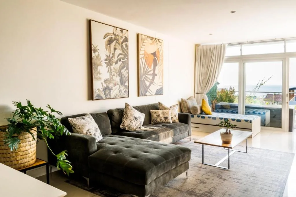 Modern lounge with dark sofa, botanical artwork, and sea view through large windows