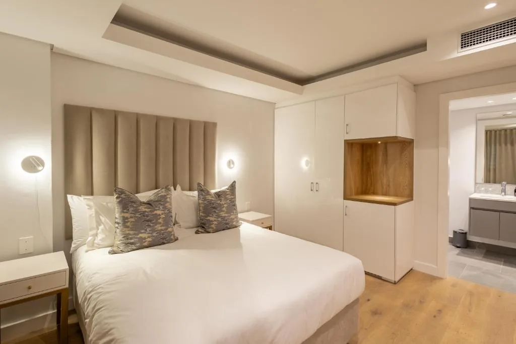 Modern bedroom with queen bed, upholstered headboard, and en-suite bathroom visible