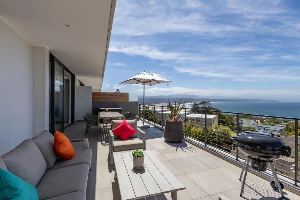 Spacious outdoor deck with seating, umbrella, and coastal ocean views