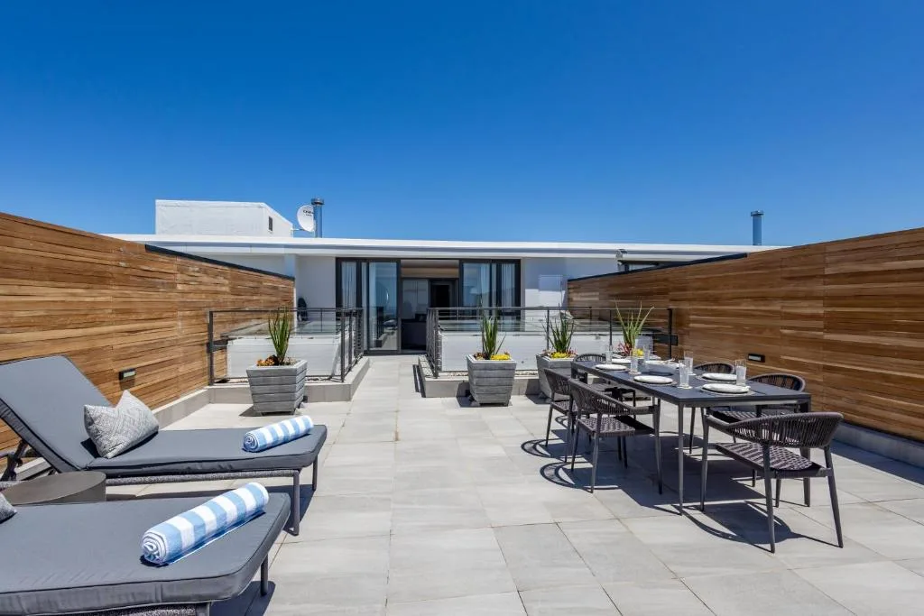 Modern rooftop deck with lounge chairs, dining table, and wooden privacy screens
