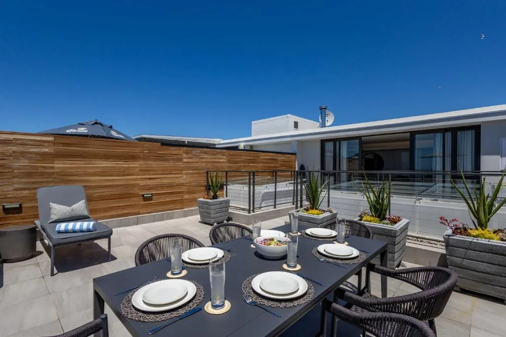 Modern rooftop terrace with dining table, lounge seating, and ocean views