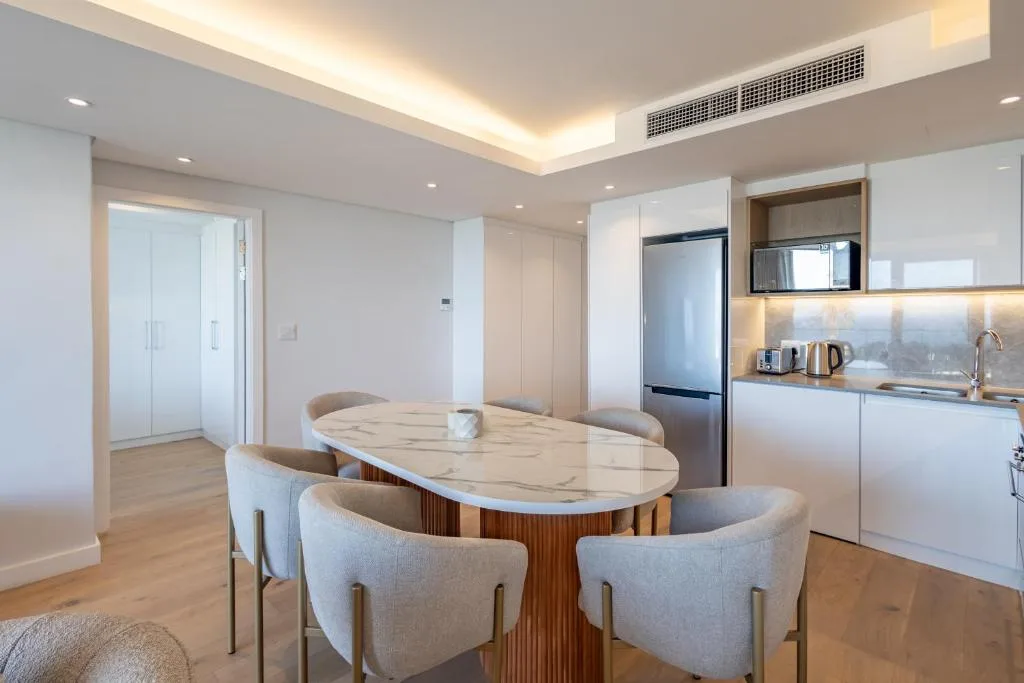 Modern dining area with marble table and cream upholstered chairs adjacent to kitchen
