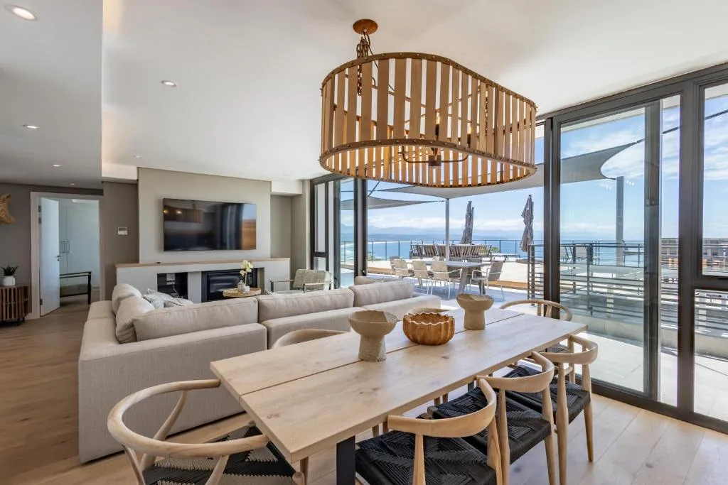 Open-plan lounge with cream sofa, dining table, and ocean views through glass doors