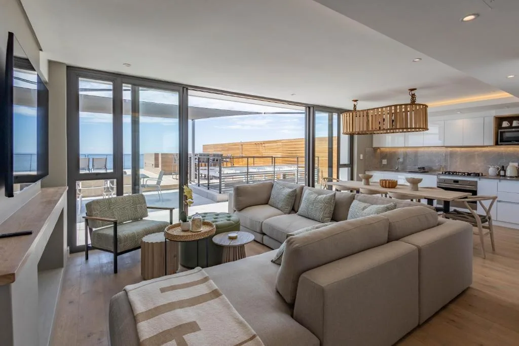 Open-plan lounge with taupe sofa, ocean view through floor-to-ceiling windows, modern pendant light