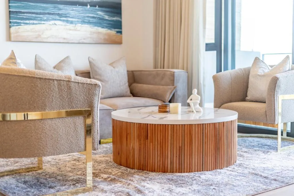 Modern lounge with beige armchairs, round wooden coffee table, ocean artwork
