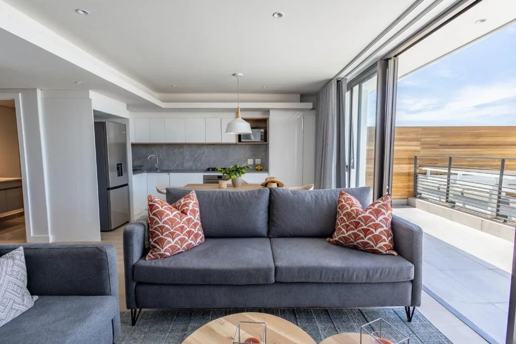 Modern lounge with gray sofa, patterned cushions, open-plan kitchen and deck view
