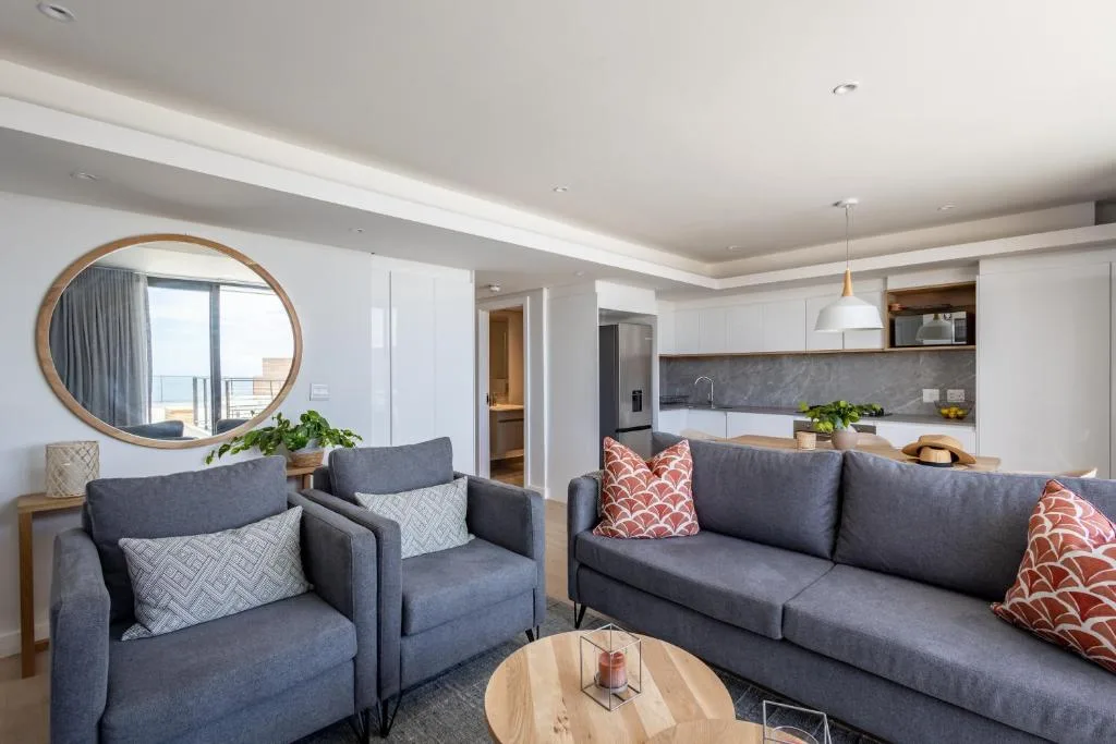 Modern open-plan lounge with grey sofas, armchairs, and kitchen visible beyond