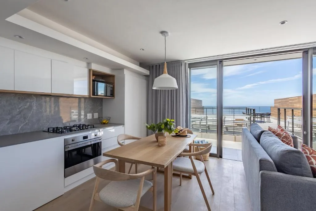 Open-plan living space with dining table, kitchen, sofa, and ocean view