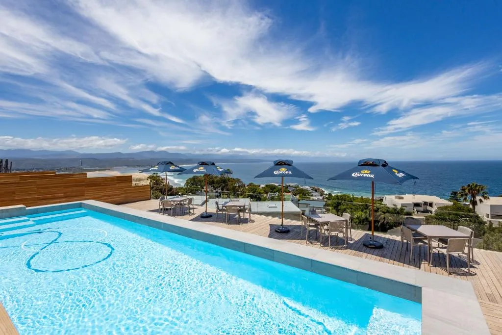 Sparkling swimming pool overlooking ocean and mountains, with deck seating and umbrellas