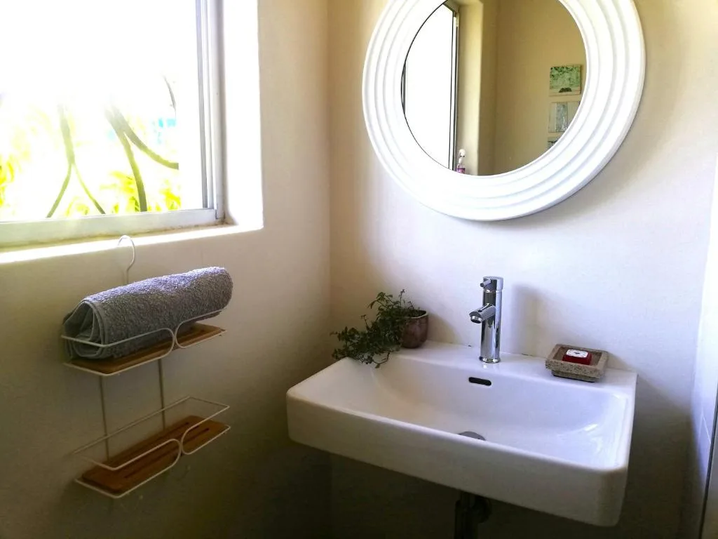 Bright bathroom with white round mirror, vanity sink, and rolled towels