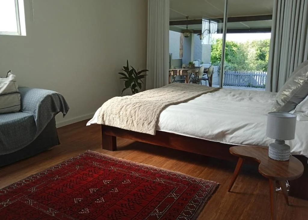 Spacious bedroom with wooden bed, red rug, and deck access overlooking garden
