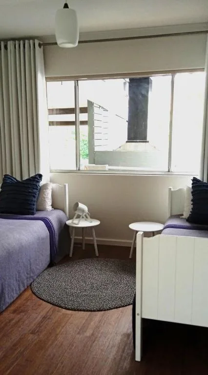 Twin bedroom with purple bedding, white pillows, round rug, and large windows