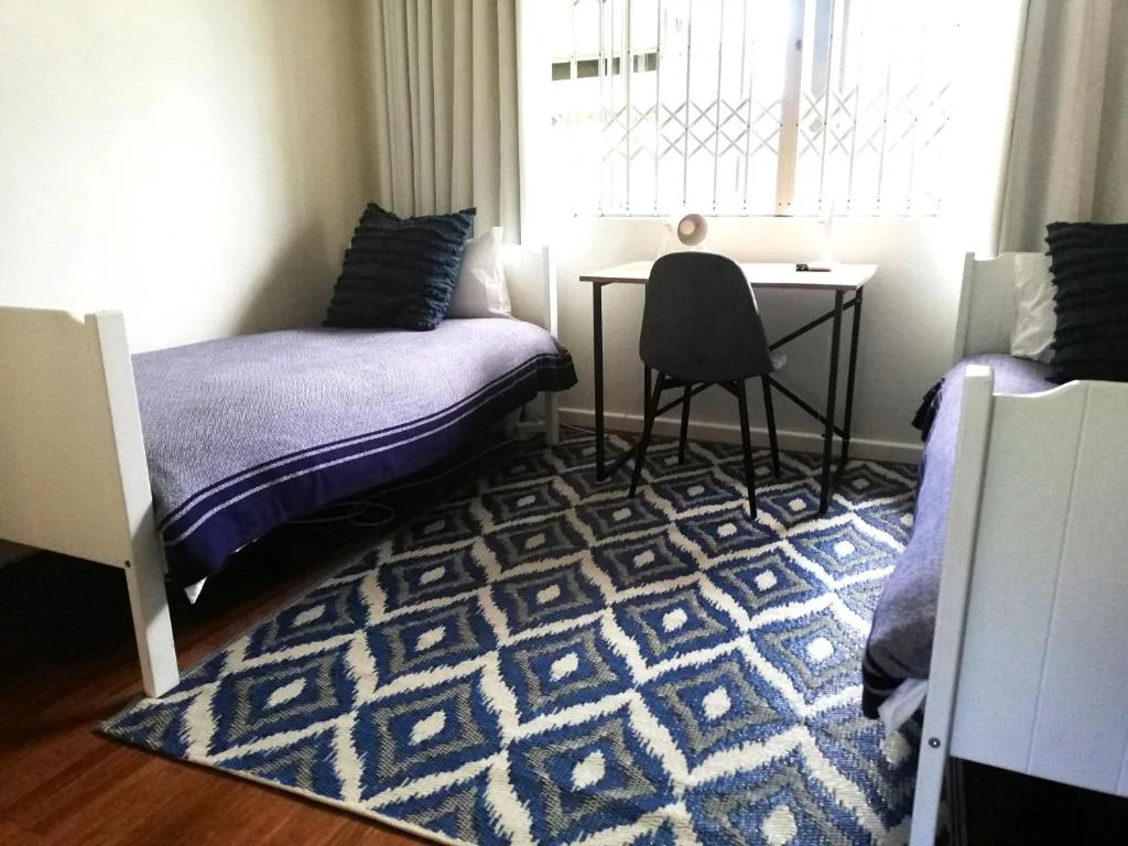 Twin bedroom with blue bedding, desk, geometric rug, and natural light