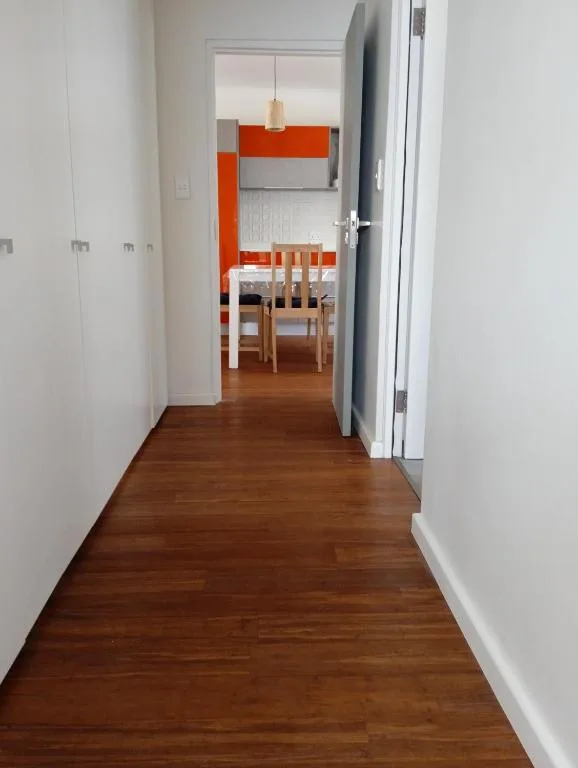 Modern hallway with wooden floors leading to orange kitchen and dining area