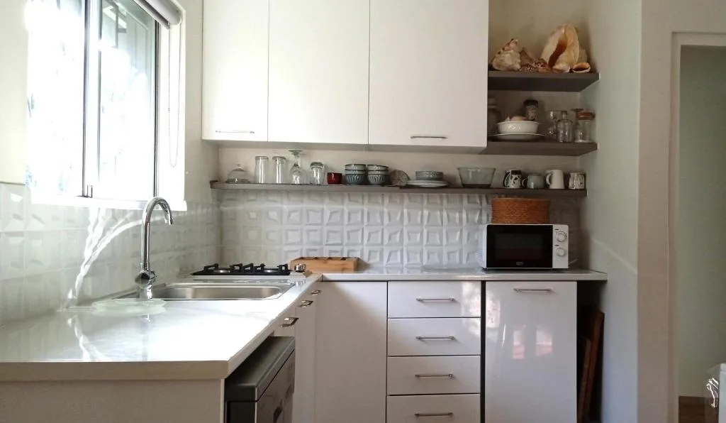 Modern compact kitchen with white cabinetry, gas stove, and open shelving