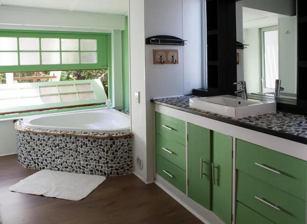 Bright bathroom with green cabinetry, soaking tub, and dual vanity sink