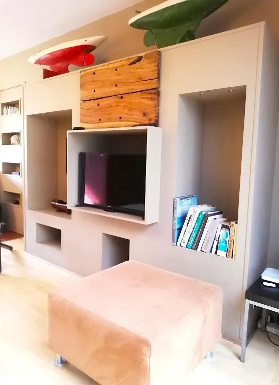 Modern lounge with built-in white shelving, TV, and decorative wooden artwork
