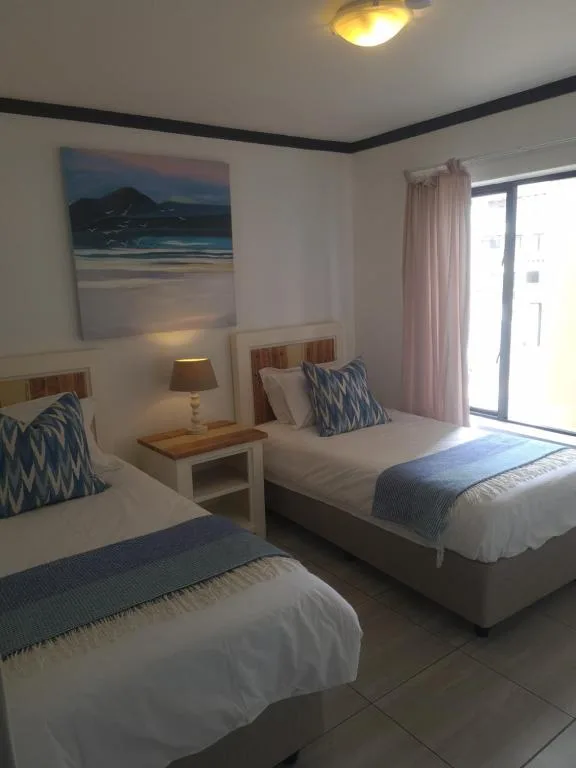 Bright bedroom with two single beds, coastal artwork, and patio doors