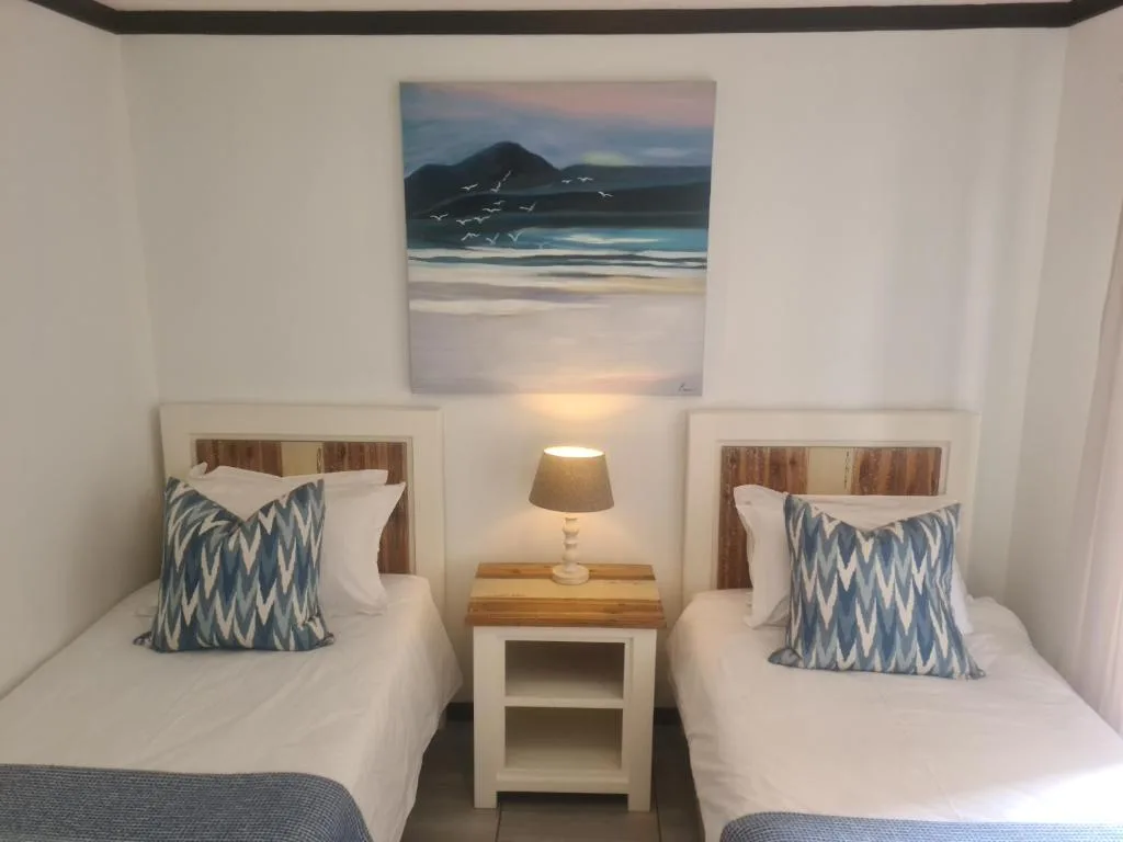Twin bedroom with white linens, patterned pillows, and coastal artwork above.