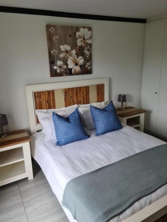 Bedroom with queen bed, blue pillows, wooden headboard, bedside tables