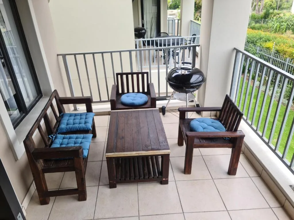 Outdoor patio with wooden chairs, cushions, braai grill, and garden views