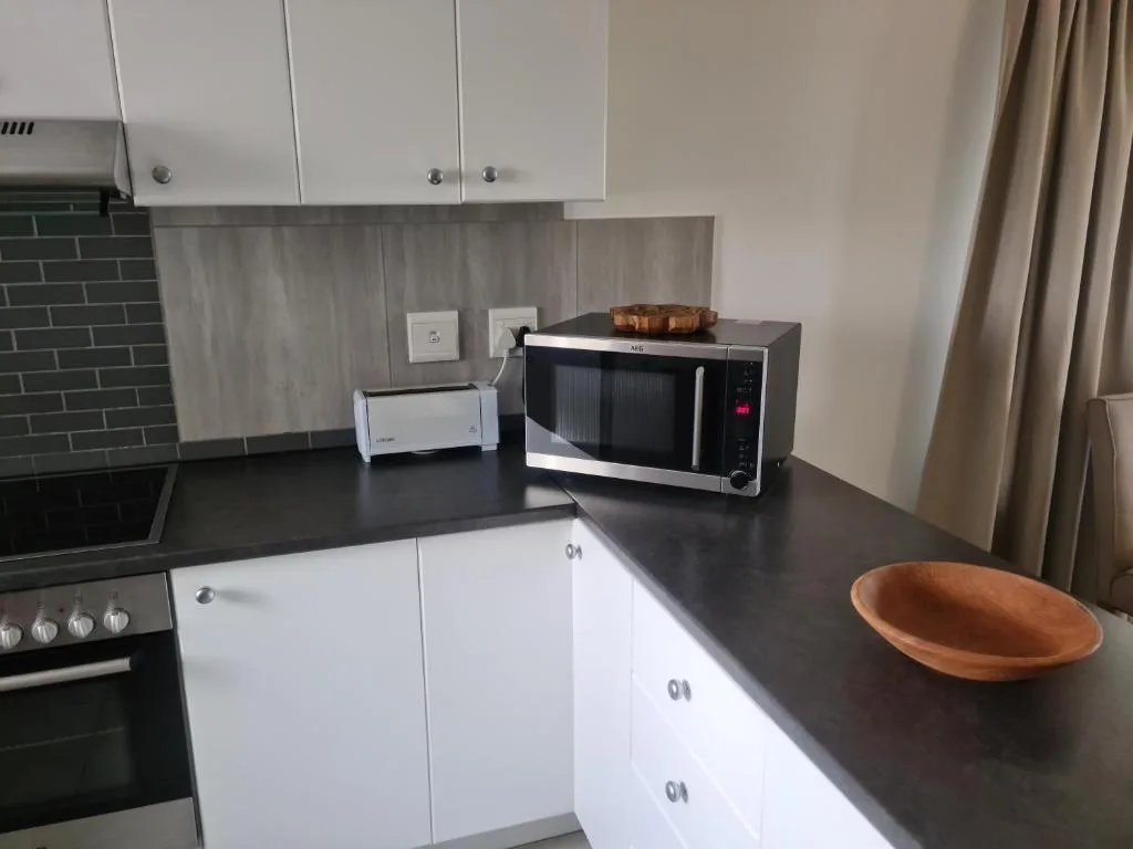 Modern kitchen with white cabinetry, dark countertop, and stainless steel microwave