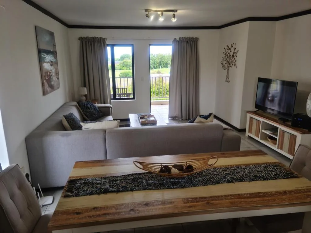 Modern living room with gray sectional sofa, TV, and garden views through glass doors